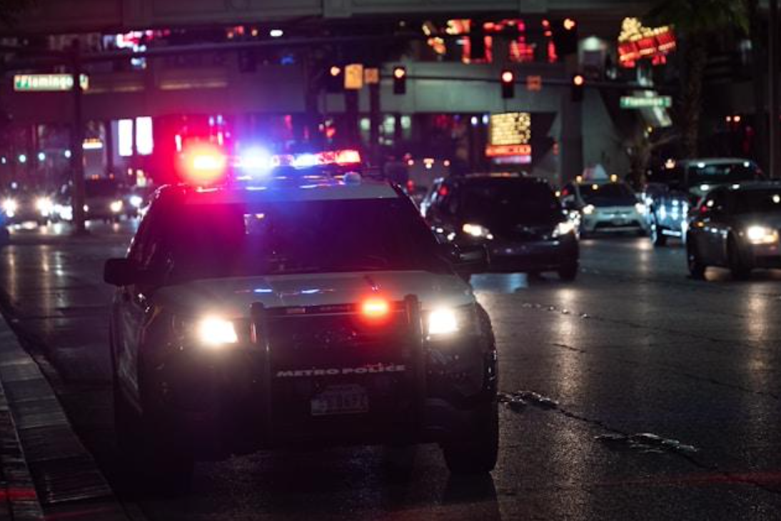 Police car with lights on pulled over at night in the city; image by Kenny Eliason, via Unsplash.com.